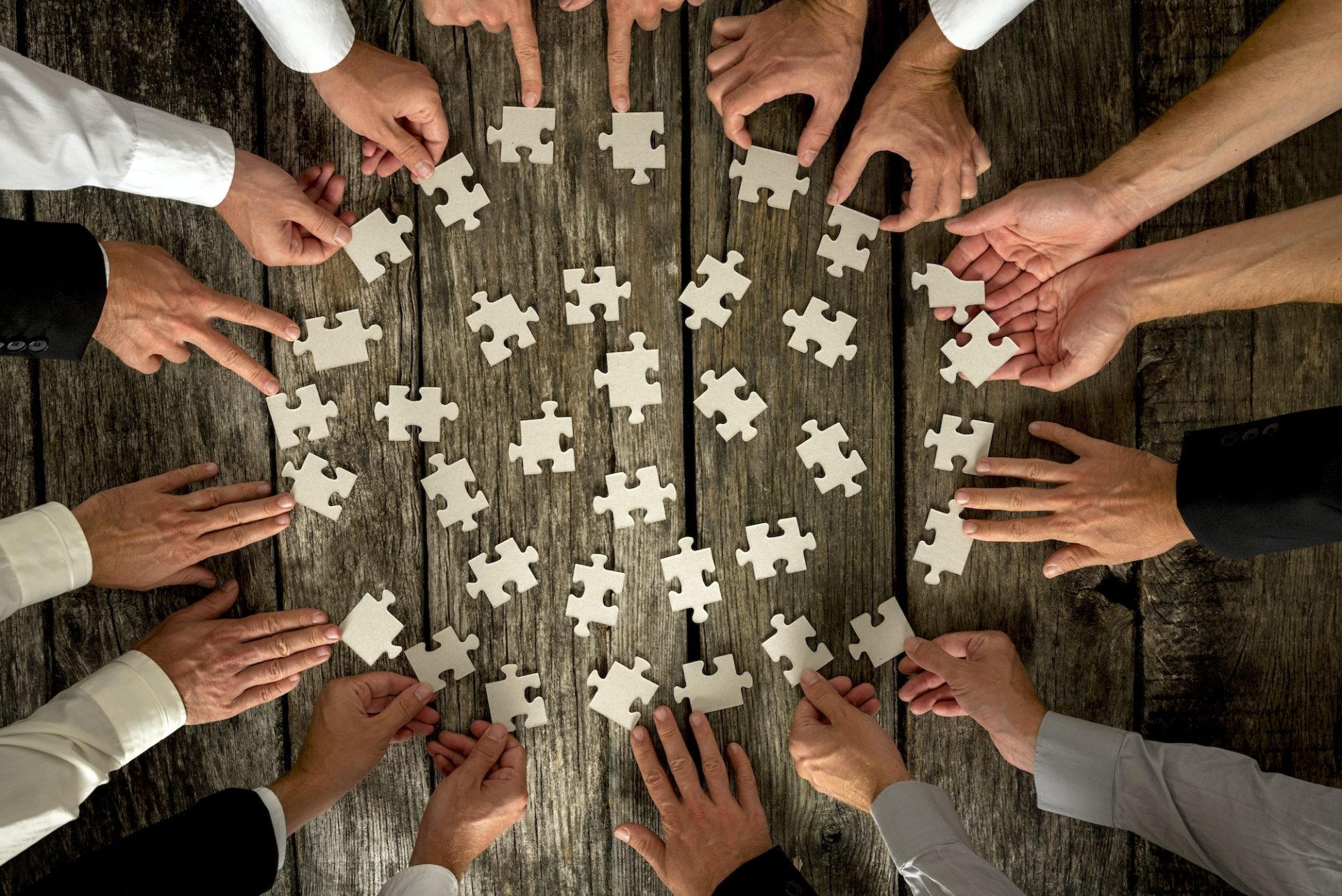 Businessmen Hands Holding Puzzle Pieces on Table