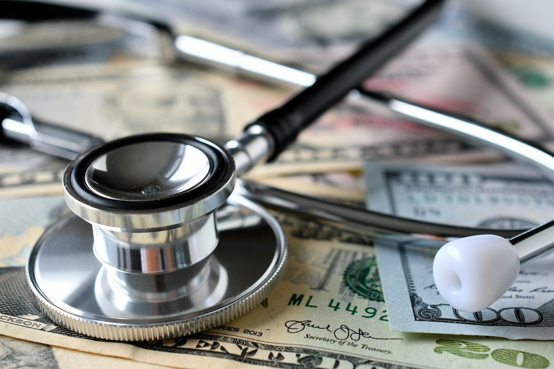 A stethoscope laying on money - the high cost of insurance. Paying healthcare expenses